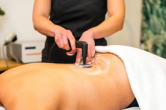 Spa therapist performing radiofrequency treatment on clients back using handheld device